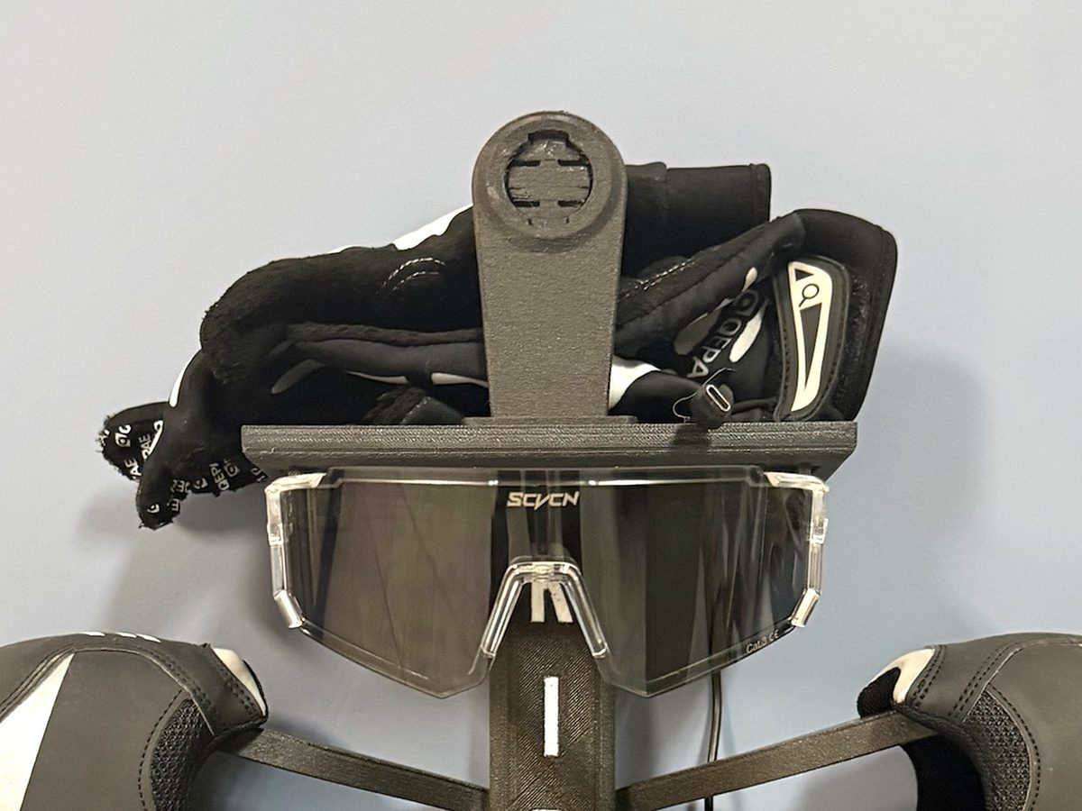 Detalle del colgador RIDE: guantes en la bandeja, gafas en las presillas y soporte para el ciclocomputador